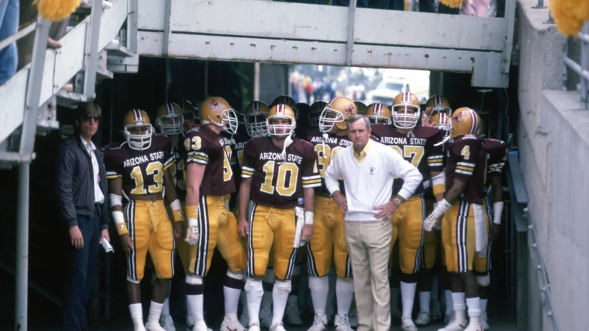 A coach stands with his football team as they wait to run onto the field.