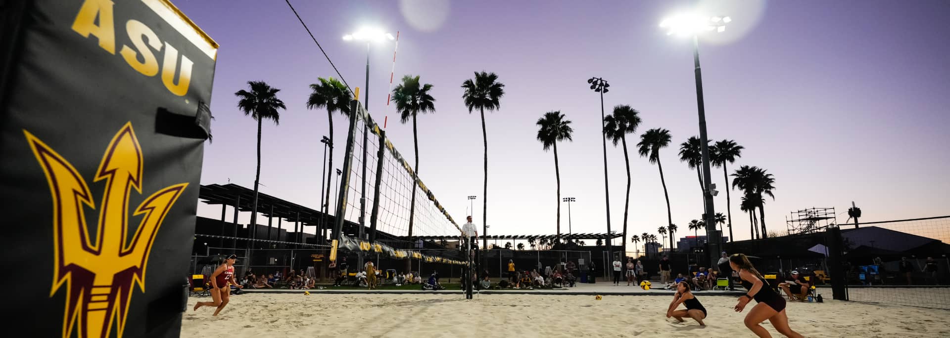 A zoomed out photo of a volleyball game going on. Two ASU volleyball players lunge for the volleyball on their side of the court.