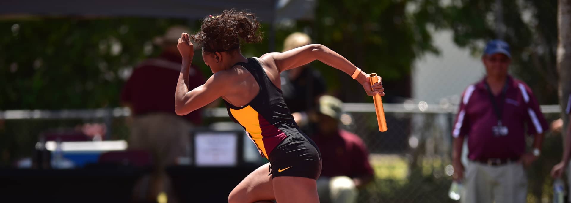 An ASU student athlete running in a relay race, wearing a maroon, gold, and black jersey