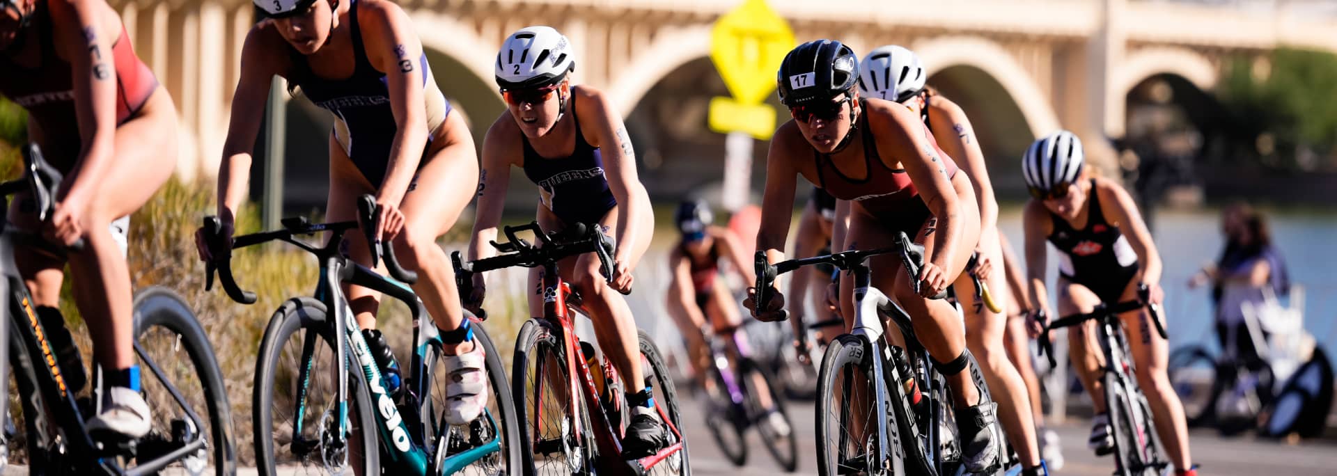 A group of student athletes are shown riding bikes in the middle of a triathlon event.