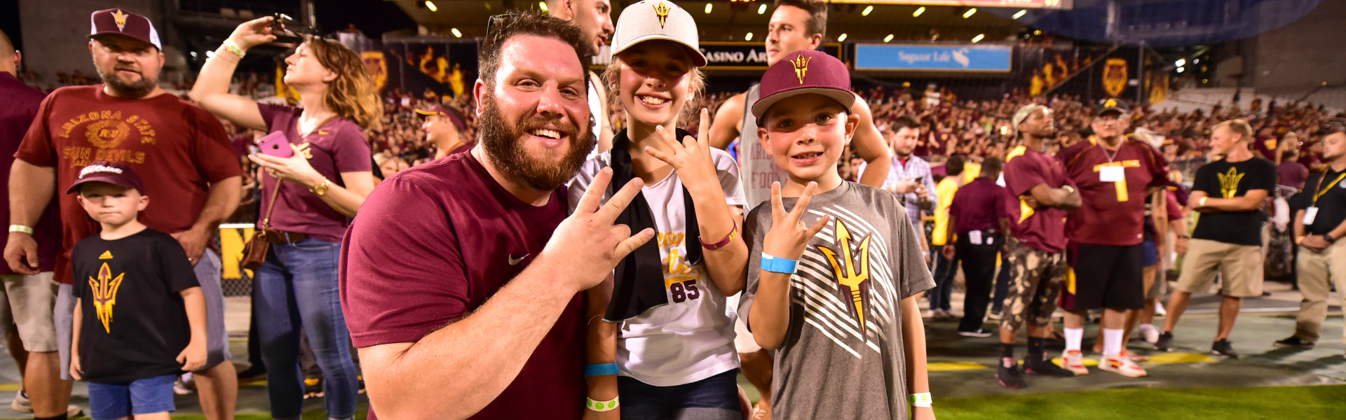 Sun Devil dad and two kids holding up the ASU hand pitchfork on the field.