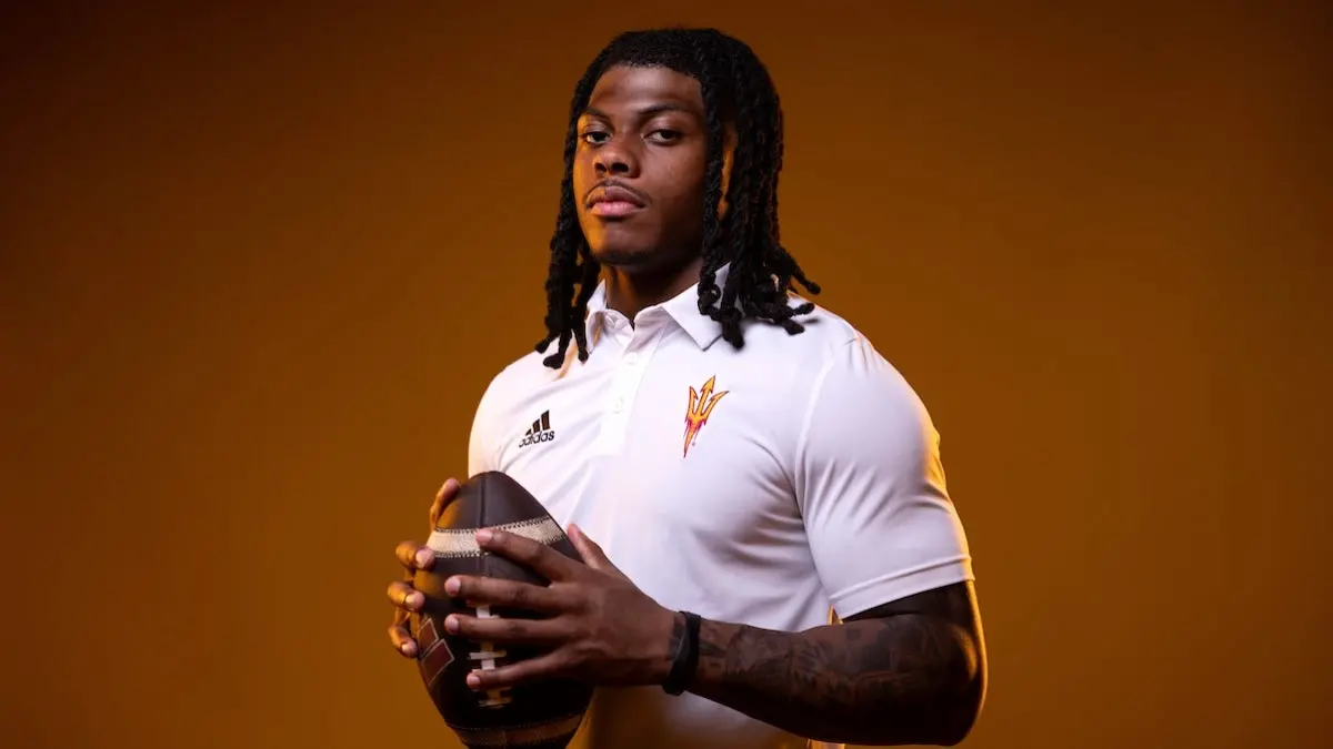 ASU running back Kyson Brown wearing a white polo with an ASU pitchfork on it and holding a football. ASU running back Kyson Brown wearing a white polo with an ASU pitchfork on it and holding a football.
