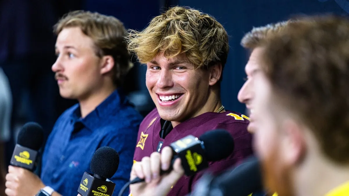 Young man in football uniform with blonde hair smiles at reporters during an interview Young man in football uniform with blonde hair smiles at reporters during an interview