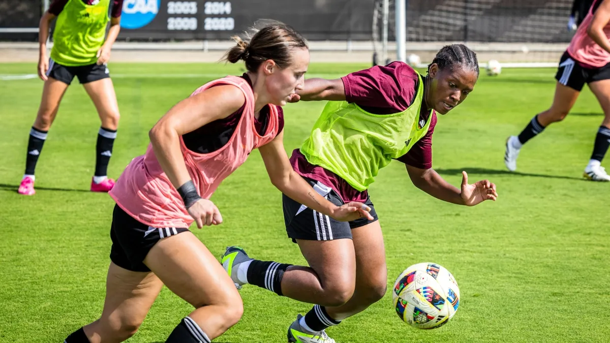 Two female college soccer players running after the ball during practice Two female college soccer players running after the ball during practice