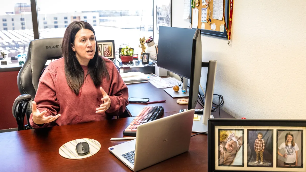 A woman seated at a desk speaks to someone off camera