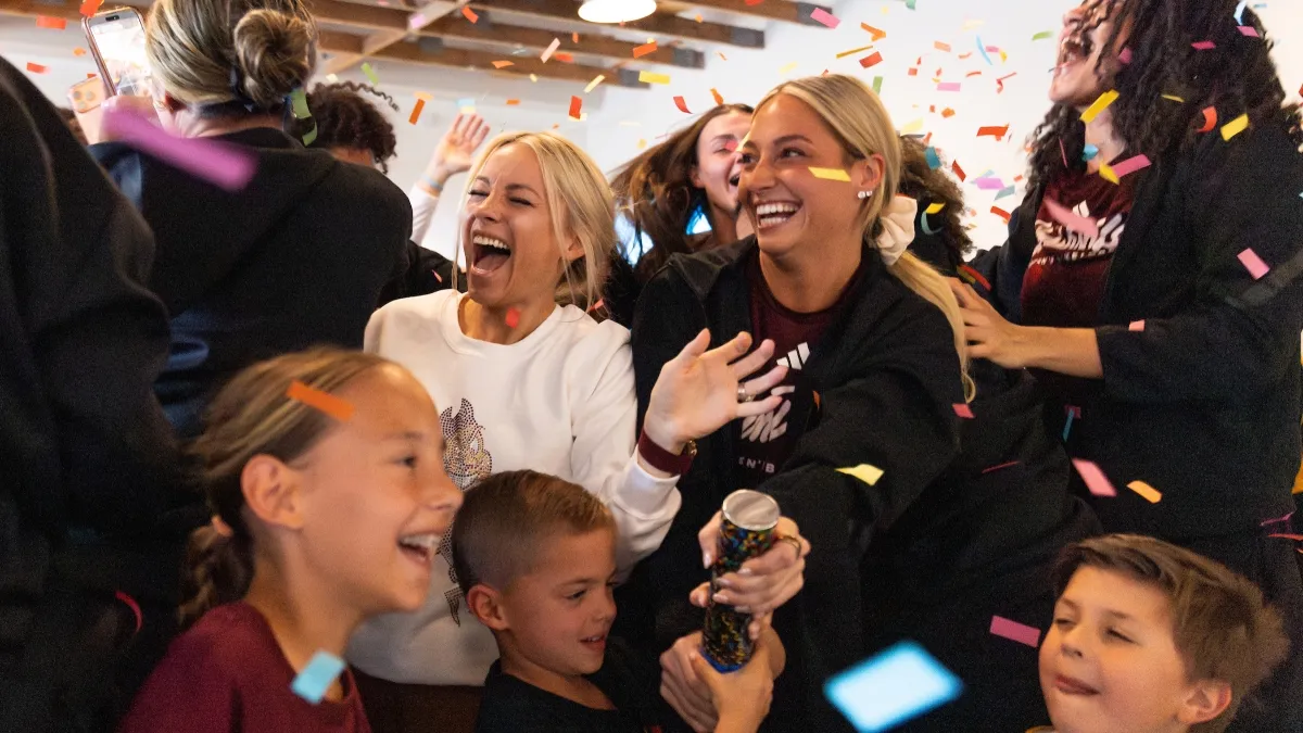 A group of women and children smile and celebrate with confetti flying around them
