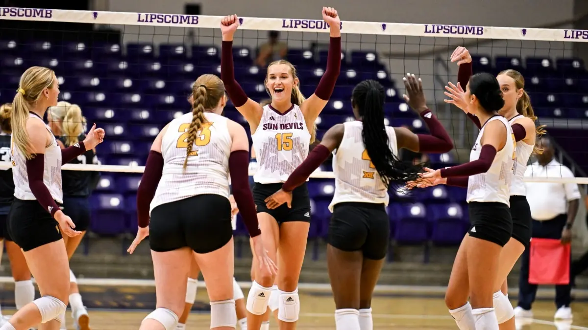 Photo by: Reily Rogers Volleyball team cheering by net with one girls arms up in happiness