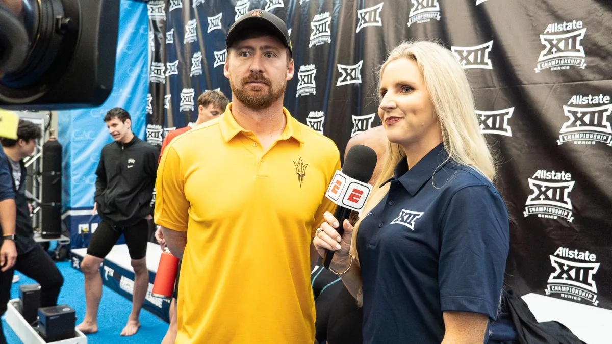 A man in a baseball cap and gold ASU polo is interviewed by a woman wearing a Big 12 polo