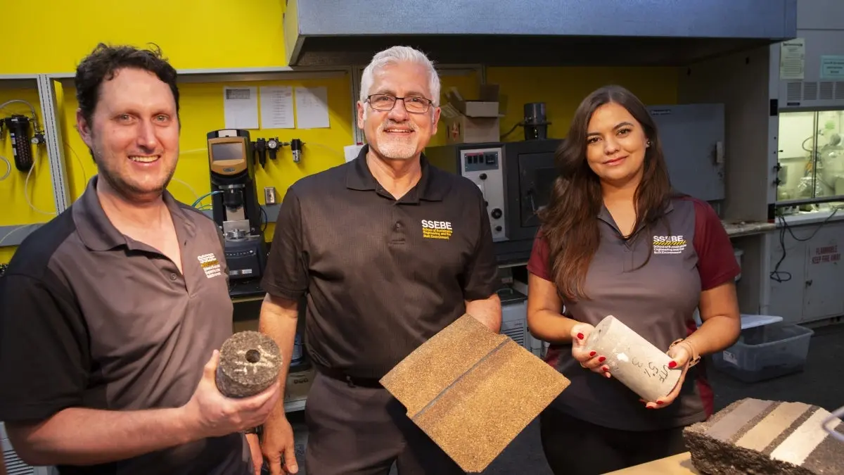 Three people standing in a lab holding items made out of various construction materials. Three people standing in a lab holding items made out of various construction materials.