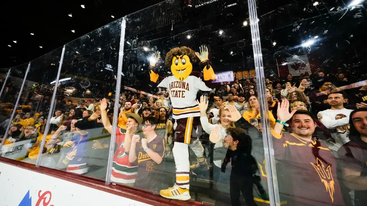 Sparky standing on the glass in student section at Mullett Arena