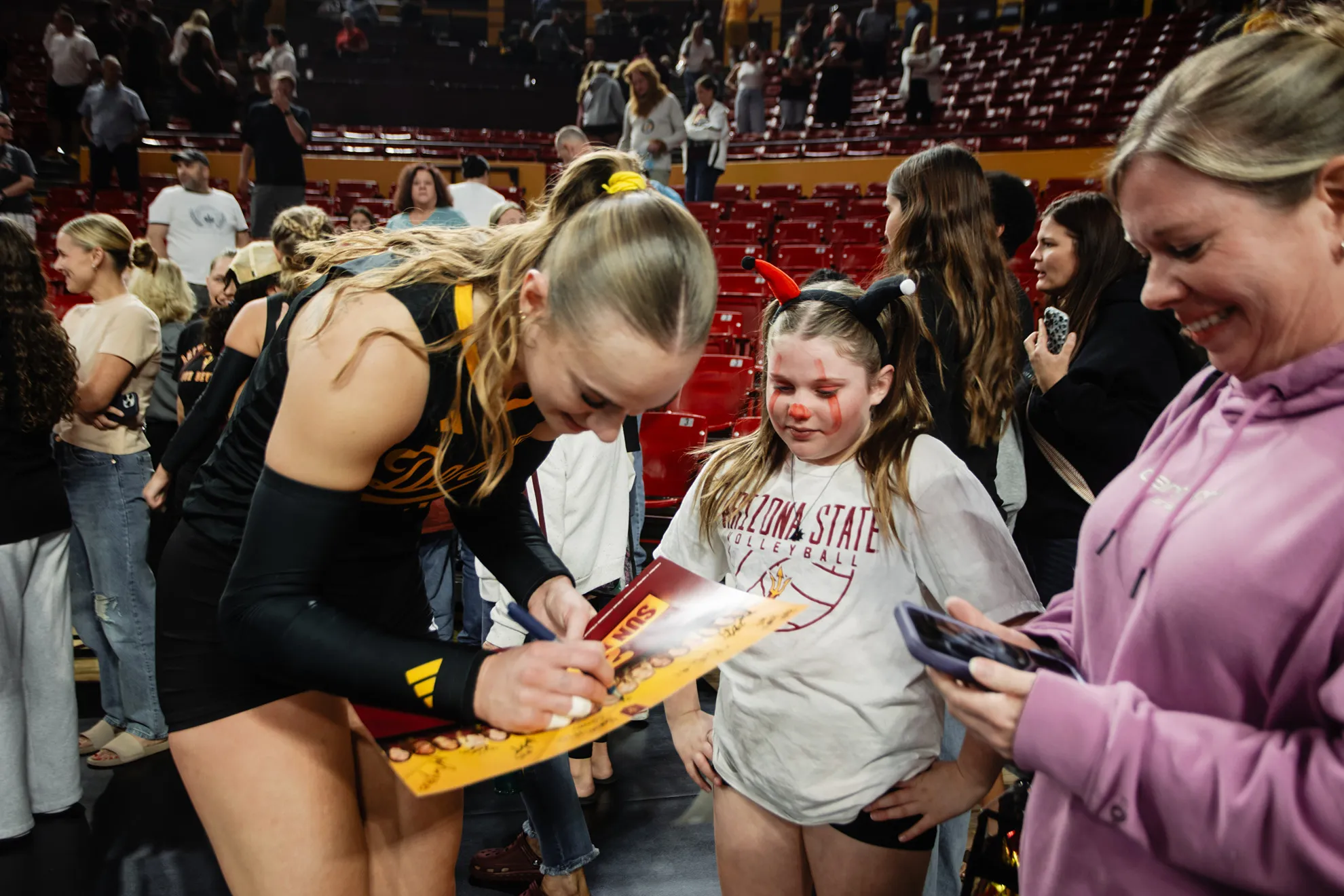 Bailey Miller signing a team poster for a fan following a volleyball match.