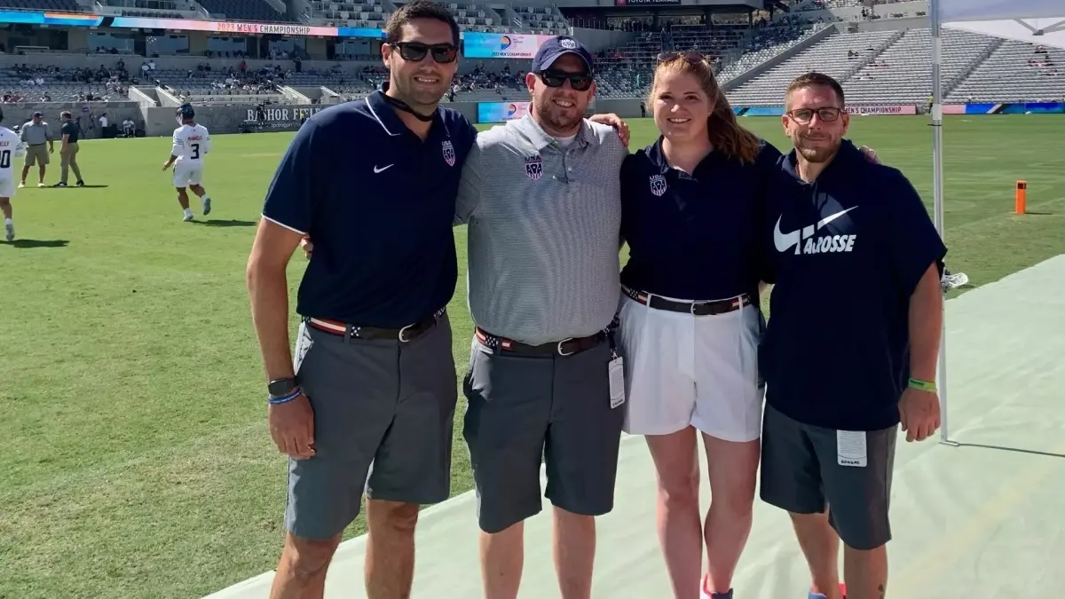 Nate Snyder (grey polo) with the support team, the team behind the team. three men and one woman posing at on the field