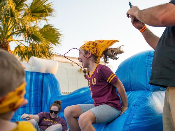 A young girl in an ASU shirt jumps in an inflatable bouncy house.