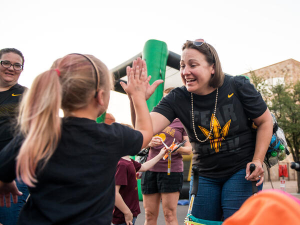 A women in an ASU branded t-shirt high-fives a young girl with a ponytail outside.