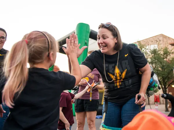 A women in an ASU branded t-shirt high-fives a young girl with a ponytail outside.