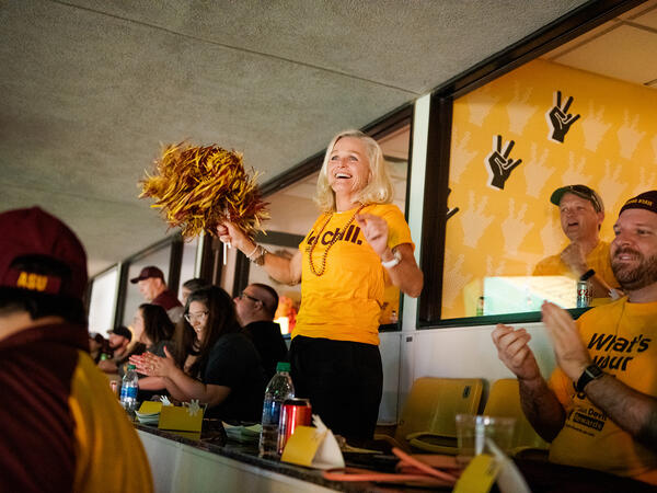 Woman cheering for ASU waving pom-poms in stadium box