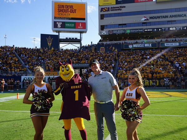 Two cheerleaders standing with man and Sparky holding up a jersey